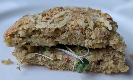 Golden vegan cheese and potato scone with roasted garlic cloves and fresh mixed microgreens.