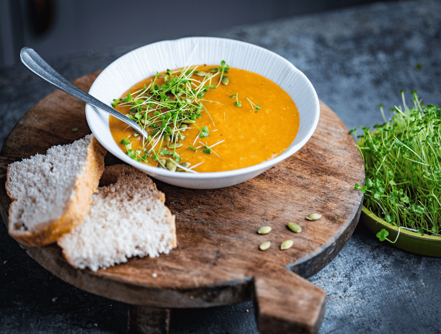 bowl of soup with bread and greens on a wooden board