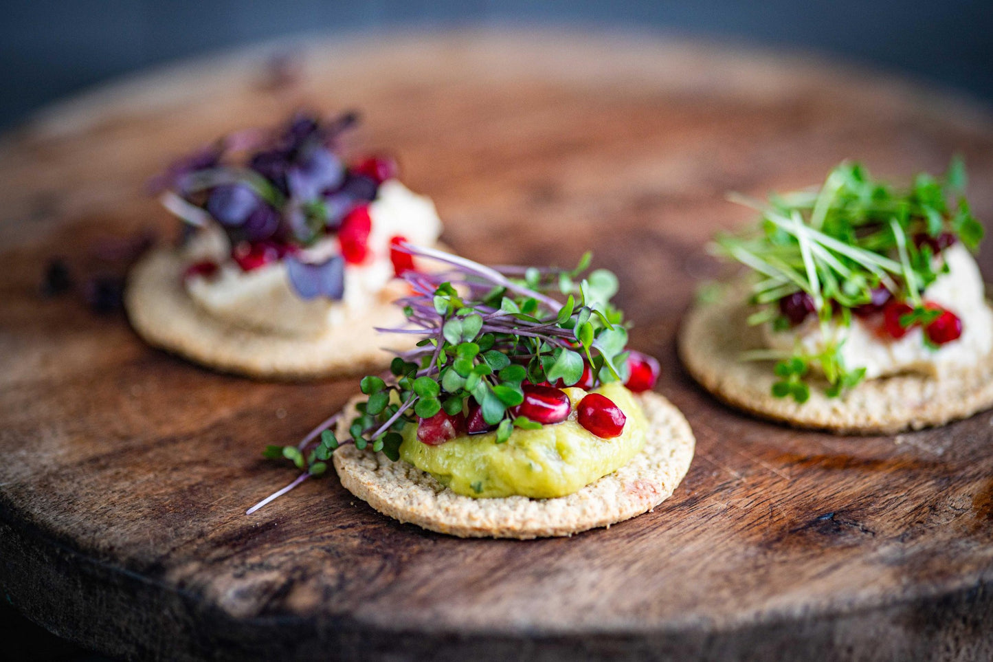 Teeny Greeny organic microgreens food styling shot with crackers hummus and pomegranate seeds on rustic wooden board