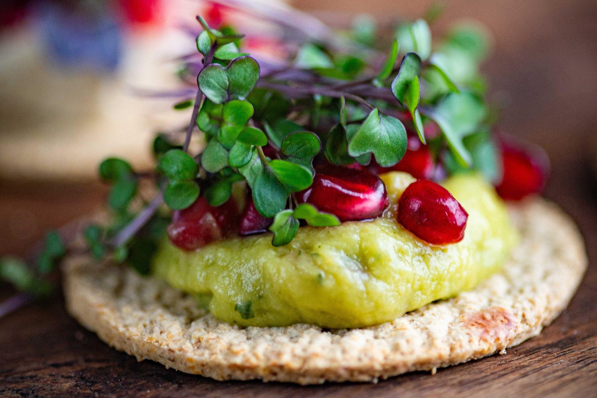 Teeny Greeny red cabbage microgreens on oat cracker with avocado and pomegranate seeds
